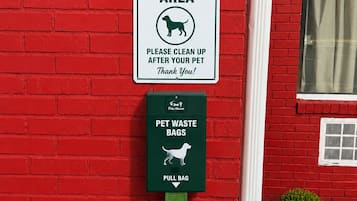 A red brick wall with a pet cleanup area sign and a pet waste bag dispenser.