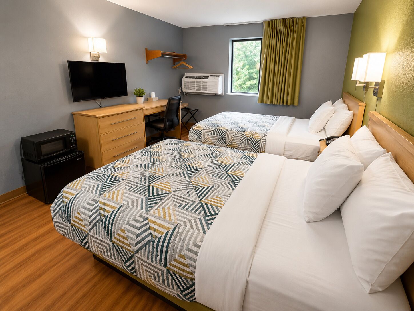 A hotel room with a bed, a desk, a chair, a television, an air conditioner, and a window with curtains.