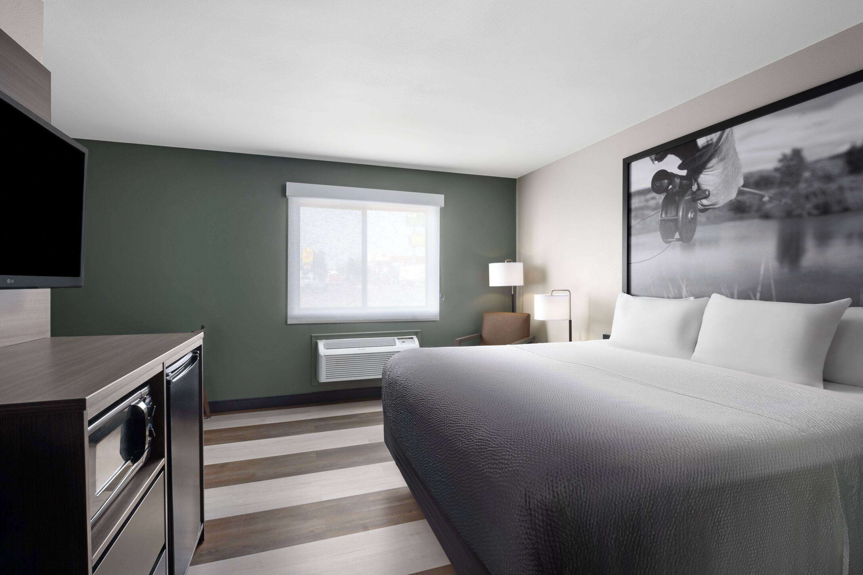 A hotel room with a bed, a television, a window, and a wall-mounted air conditioner.