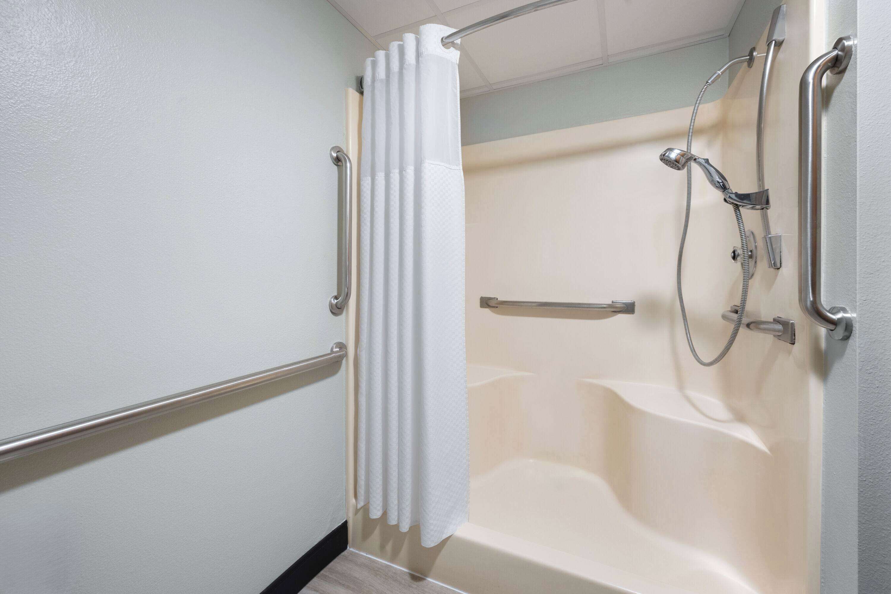 A bathroom with a bathtub, a shower, and a handrail.