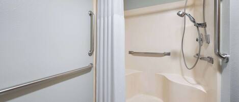 A bathroom with a bathtub, a shower, and a handrail.