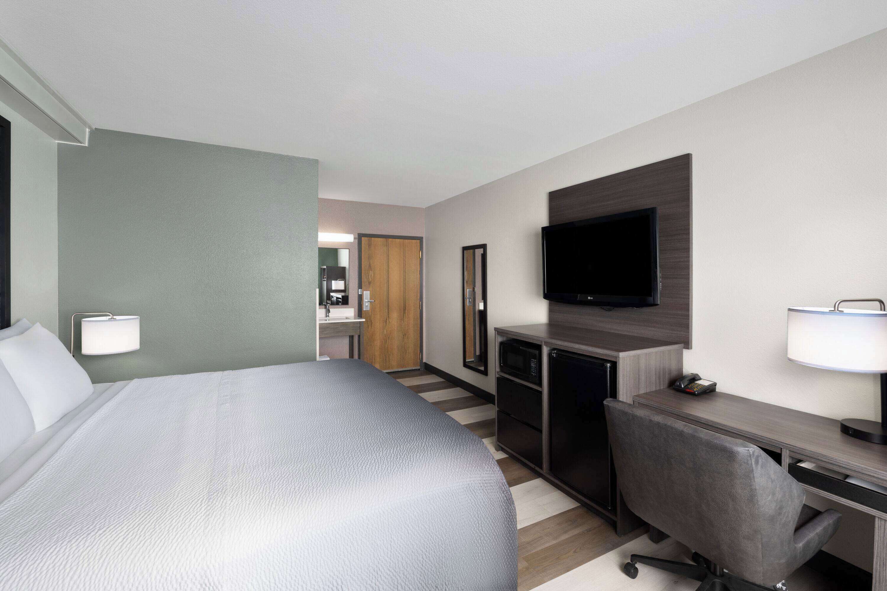 Habitación de hotel con una cama grande, un escritorio con silla, un televisor de pantalla plana y un espejo.