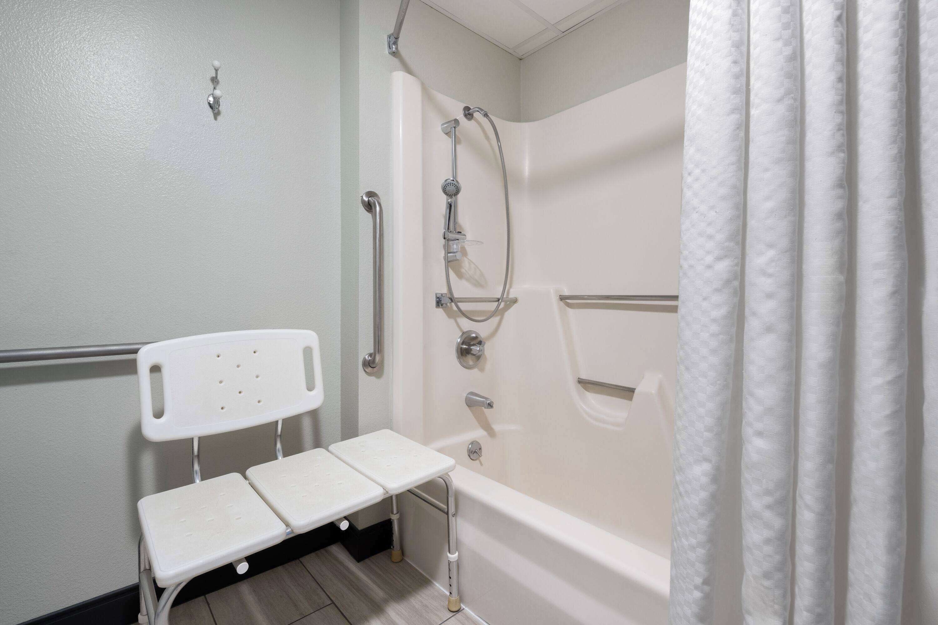 A bathroom with a white bathtub, a shower, and a white bench.
