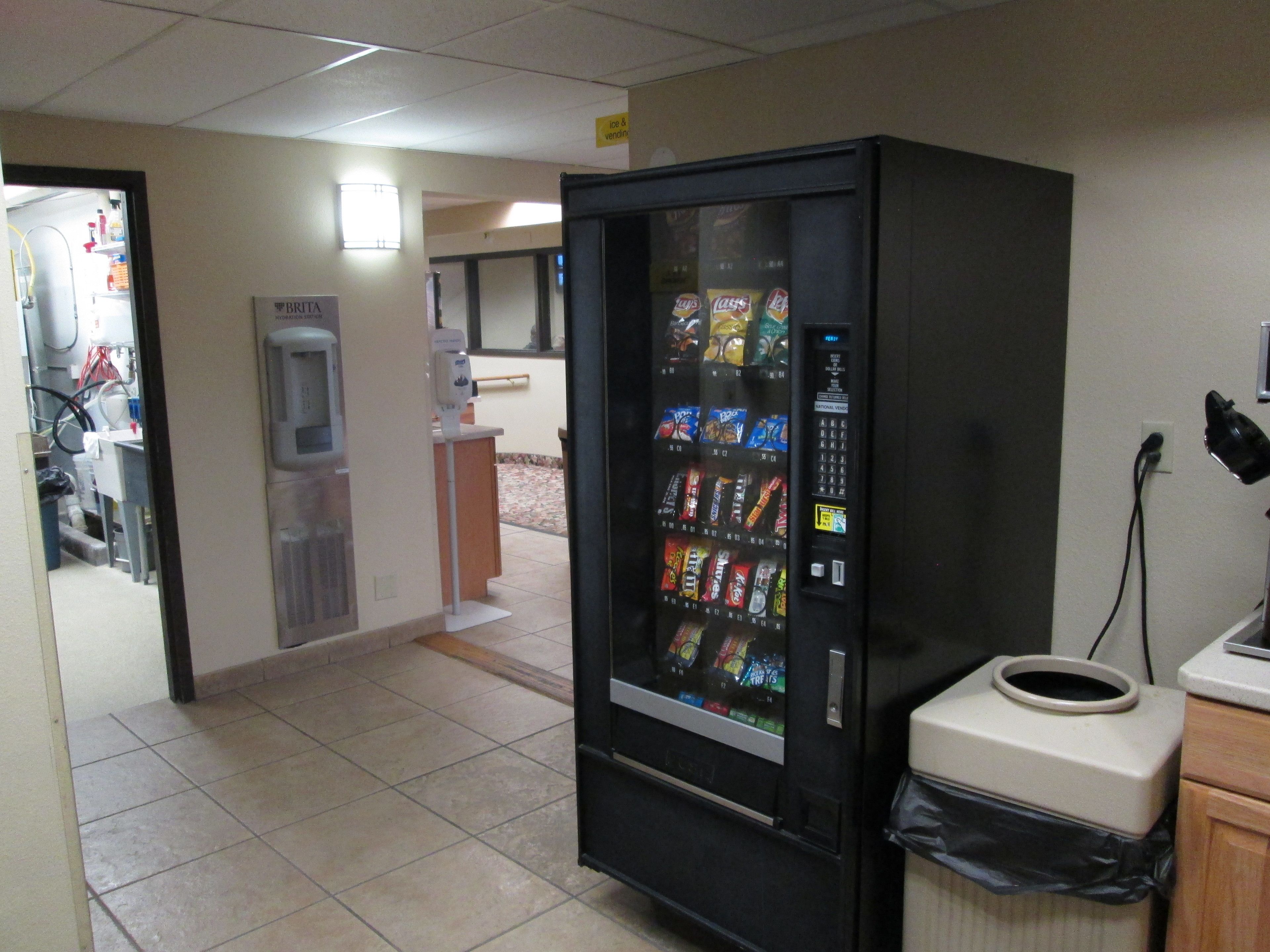Distributore automatico con diverse opzioni per snack, un cestino e un erogatore d'acqua in un corridoio.