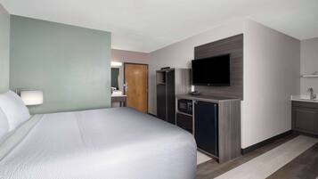 Habitación de hotel con una cama, un televisor montado en la pared, una kitchenette con microondas y una puerta de madera.