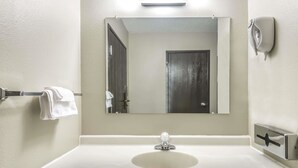 Une salle de bain avec un lavabo blanc, un miroir, un porte-serviettes et un distributeur de savon.