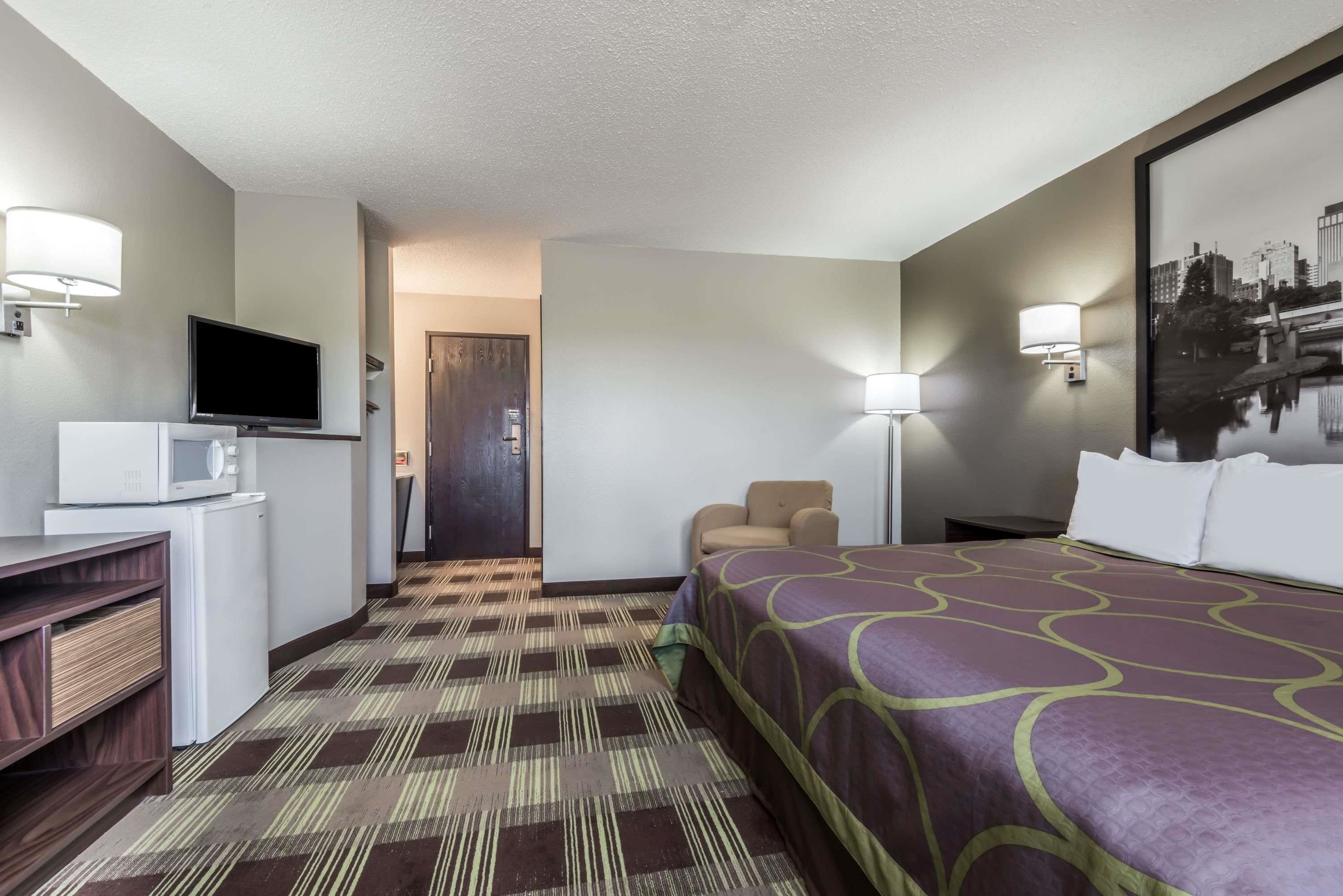 Habitación de hotel con cama, escritorio con televisor, microondas, silla y puerta que da a otra habitación.