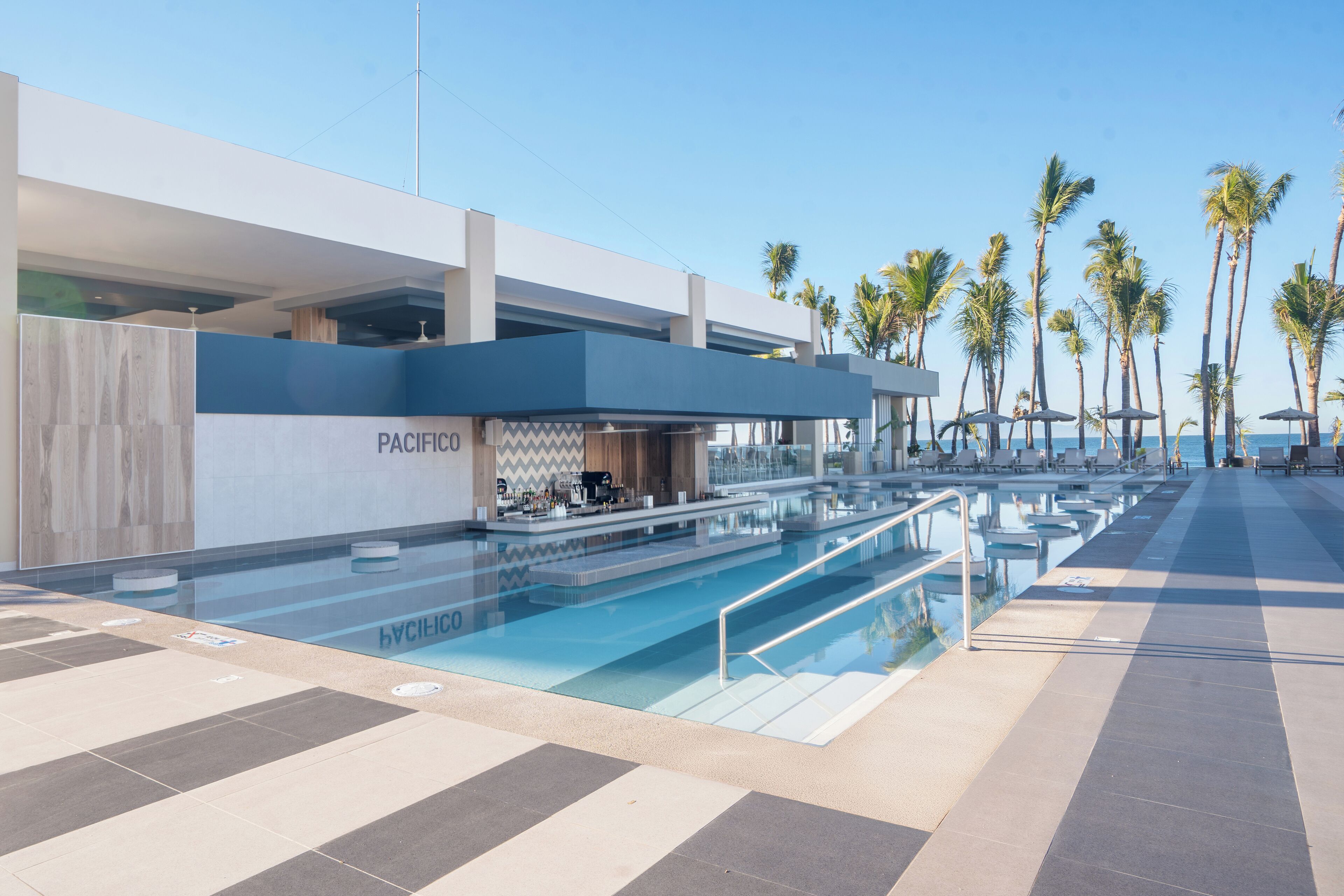A modern hotel with a pool area, palm trees, and a bar.