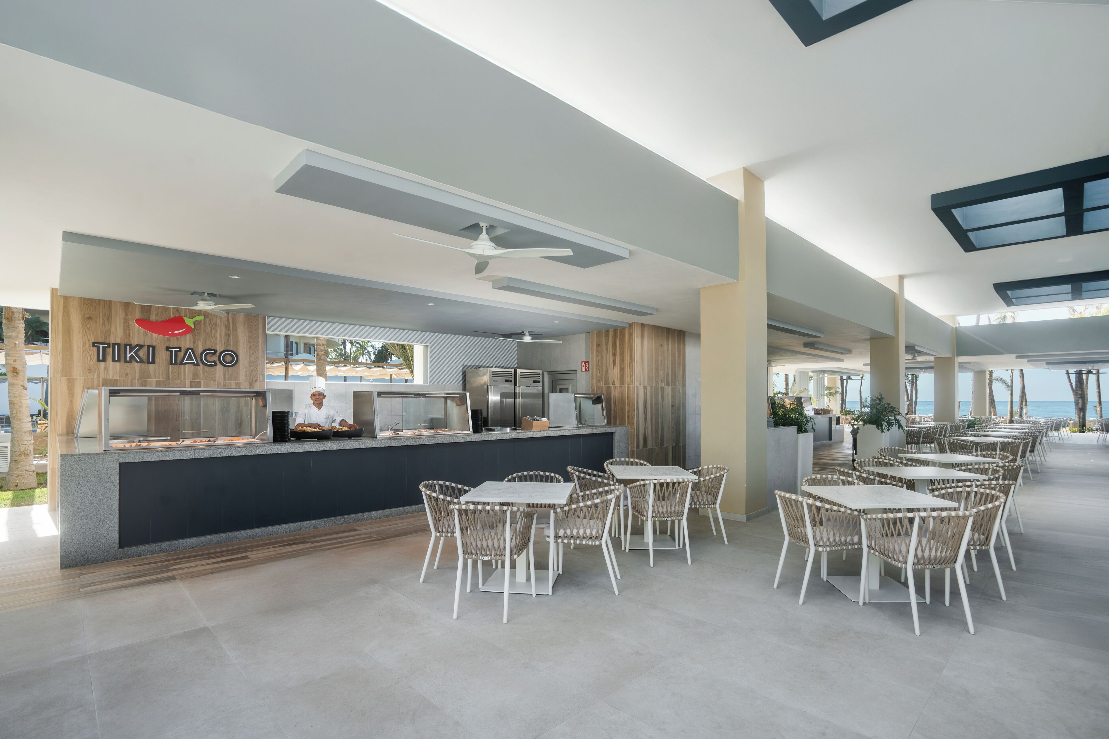 Un restaurante moderno con mostrador, sillas de mimbre blanco y vista al mar.