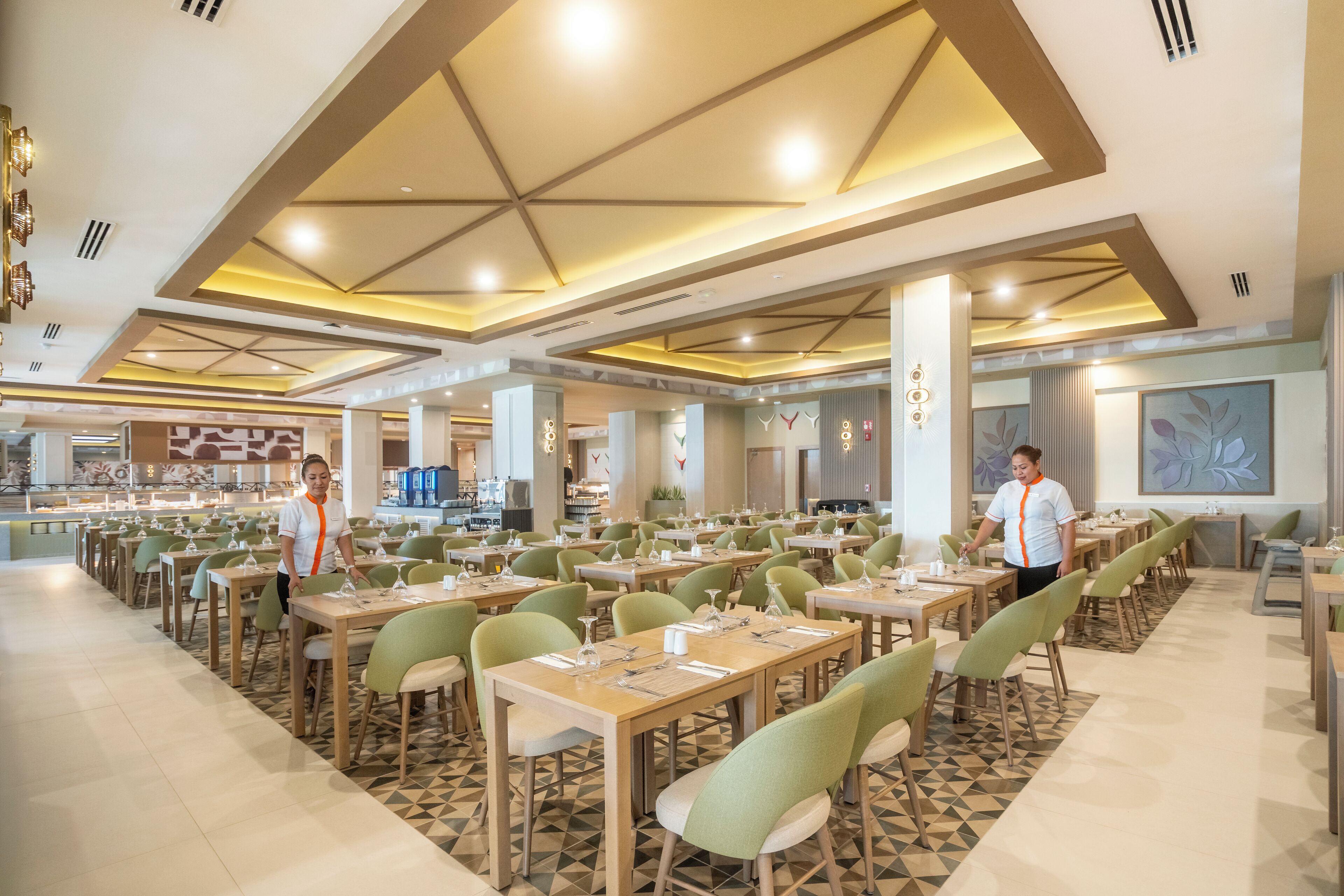 Un comedor amplio con varias mesas y sillas, una estación central de servicio y un diseño moderno en el techo.