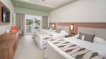 A hotel room with two beds, a desk, a TV, and a balcony with a view of palm trees.