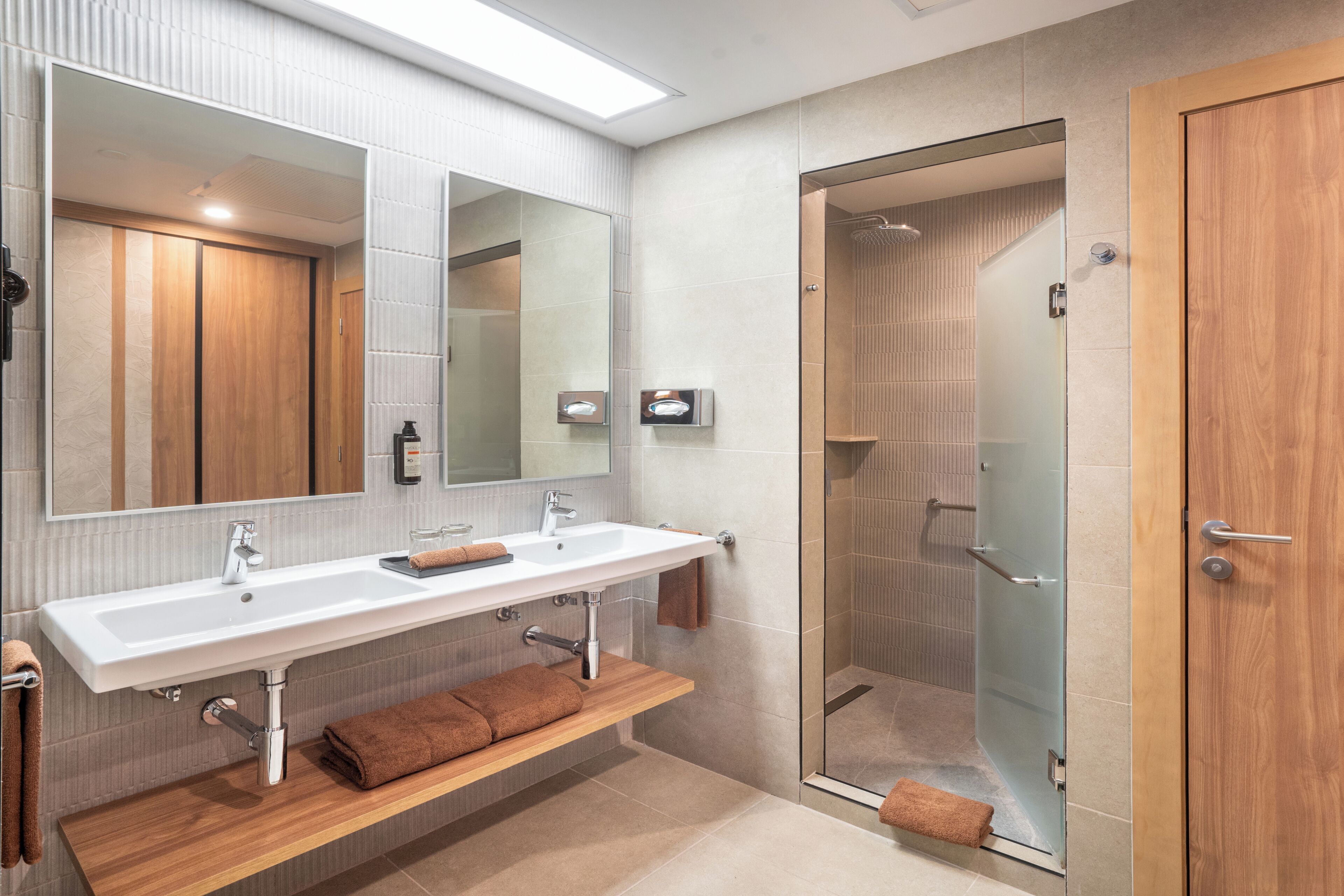 A modern bathroom with a large mirror, two sinks, a shower, and a wooden vanity.