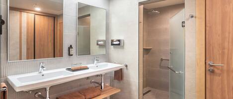 A modern bathroom with a large mirror, two sinks, a shower, and a wooden vanity.