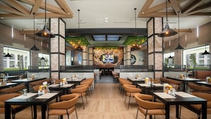 A restaurant with high tables and chairs, a brick wall mural, and hanging lights. - Riu Flamingos - All Inclusive (Nuevo Nayarit)