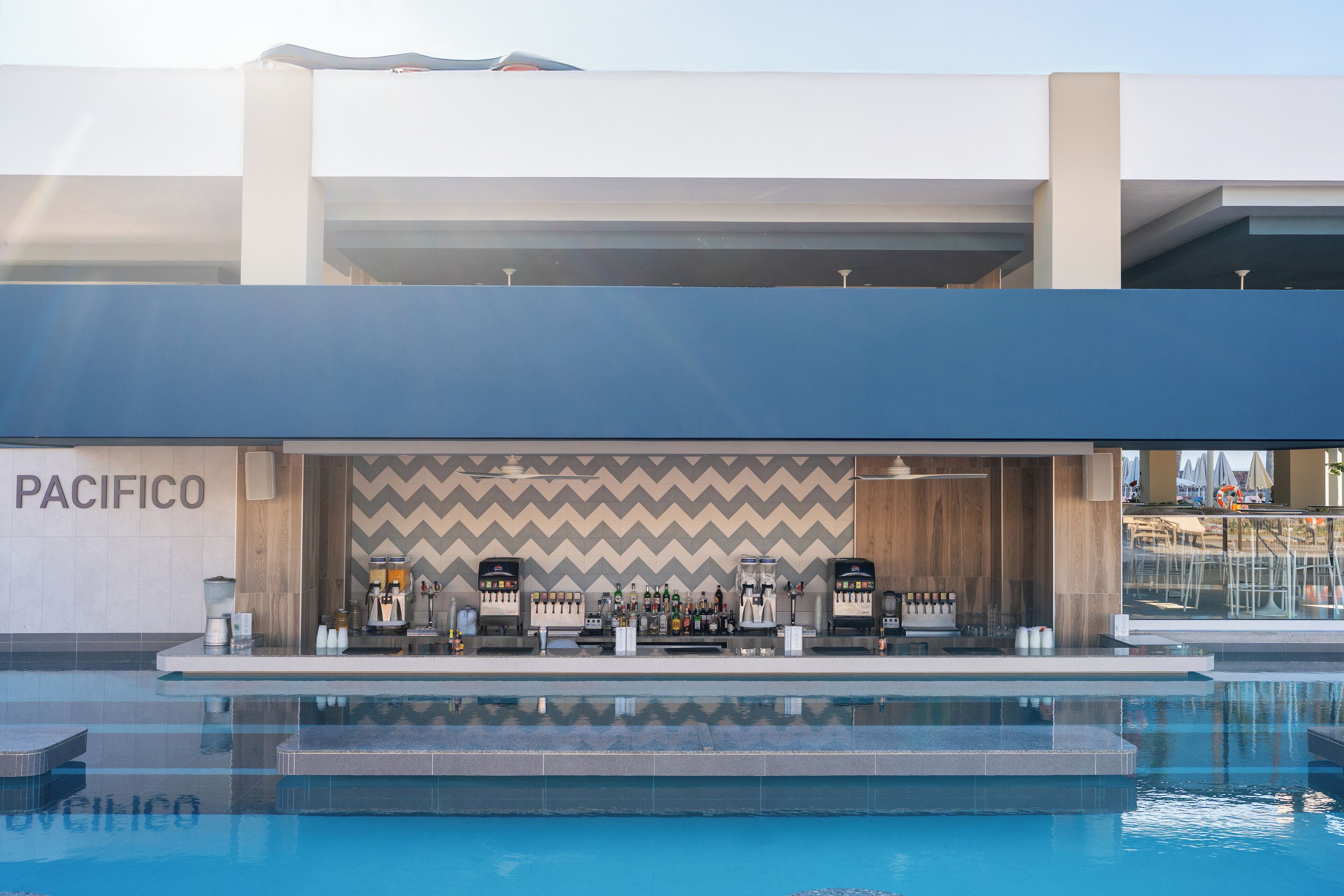 A pool area with a bar and a Pacifico sign, surrounded by a modern building with a chevron-patterned wall.