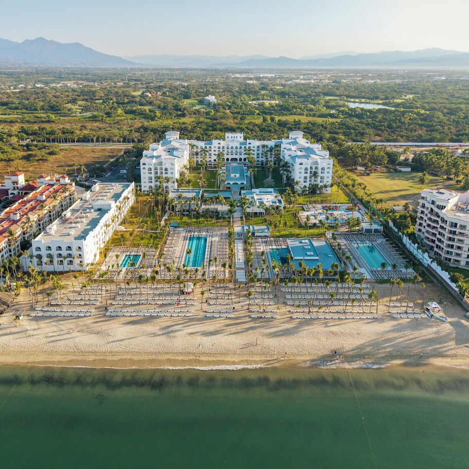 A resort with multiple buildings, a large pool area, and a beach.