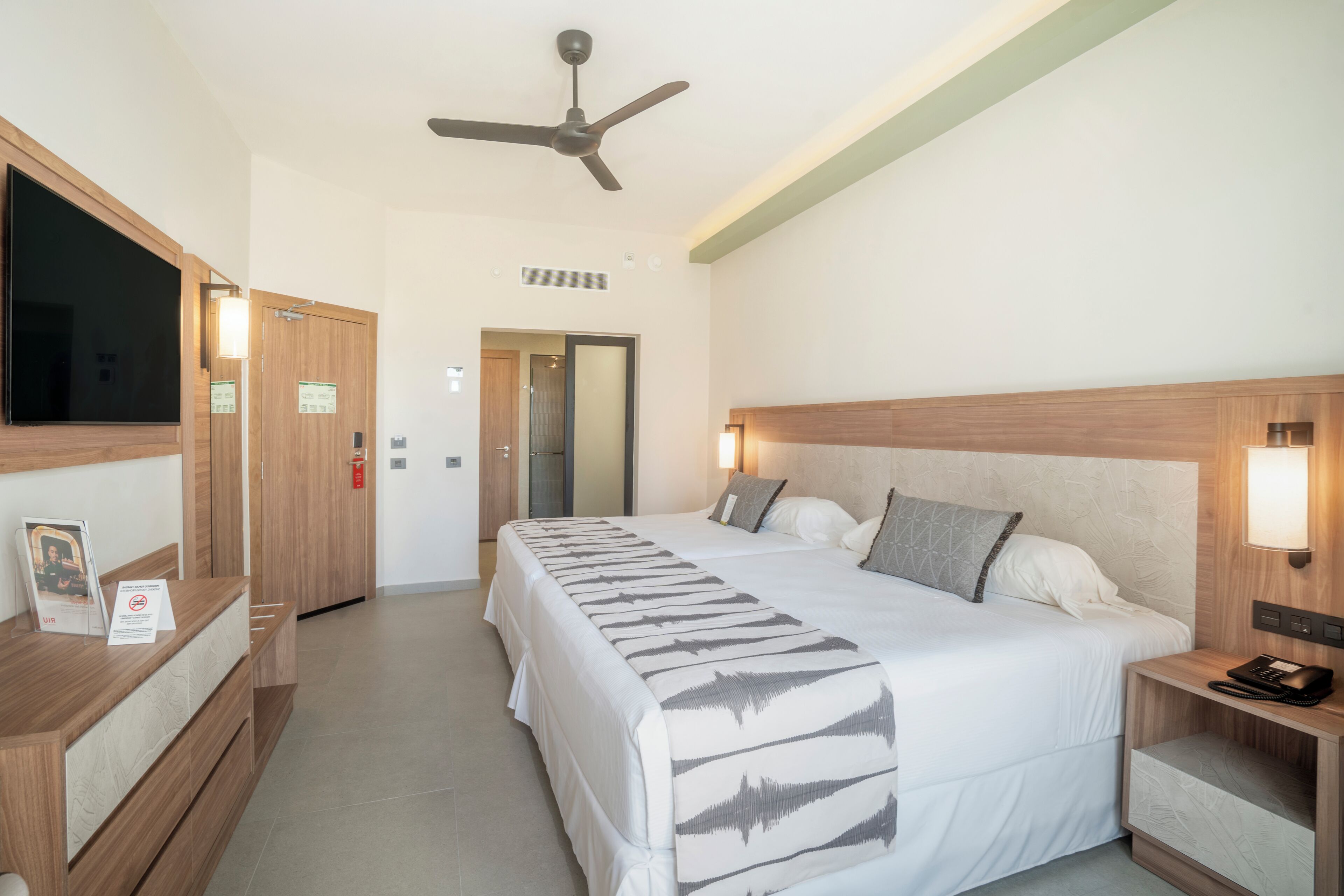 A hotel room with a bed, bedside table, nightstand, ceiling fan, and a reception desk.