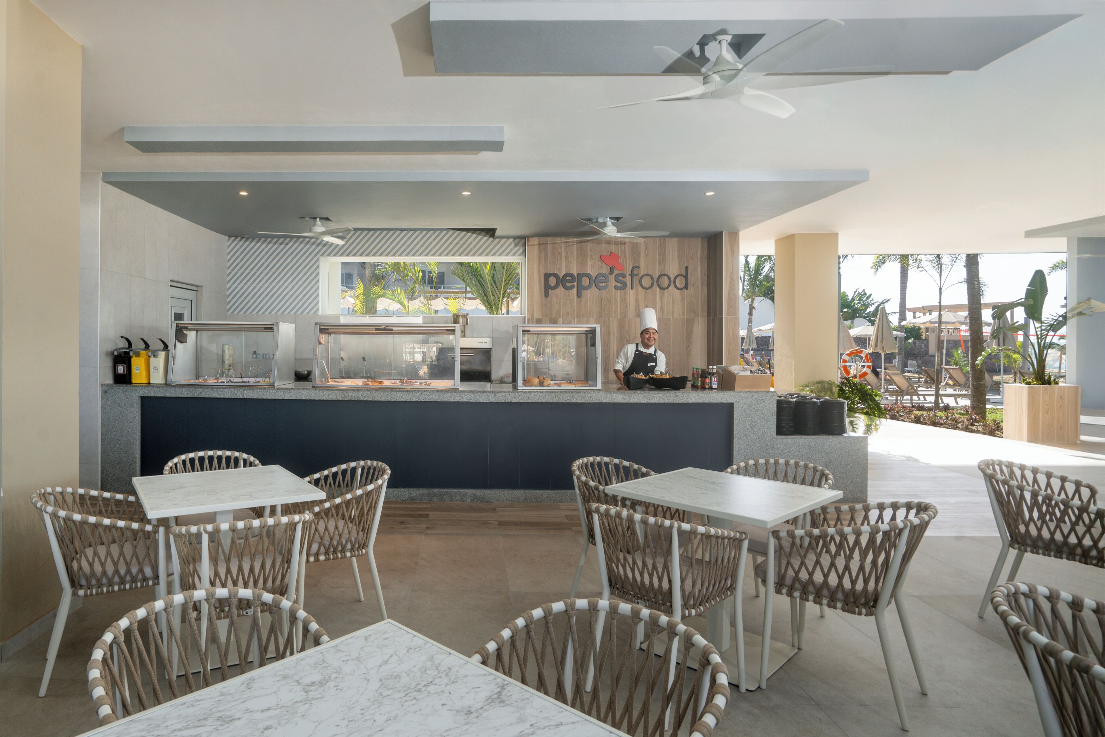 A restaurant with a counter, chef, and outdoor seating area.