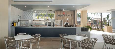 A restaurant with a counter, chef, and outdoor seating area.