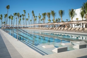A pool area with lounge chairs and umbrellas, surrounded by palm trees.