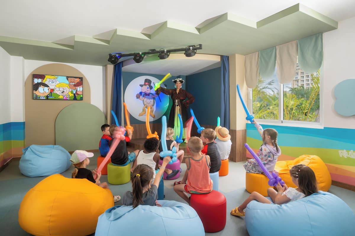A children's playroom with colorful bean bags, a stage with balloons, and a cartoon poster on the wall.