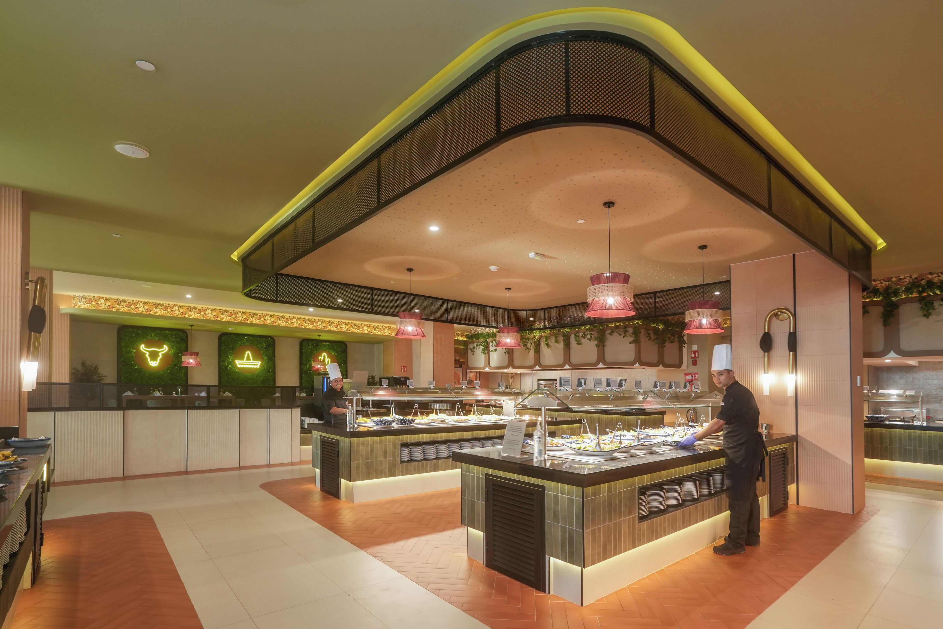 A modern restaurant with a curved ceiling, a central serving counter, and a seating area with a herringbone floor pattern.
