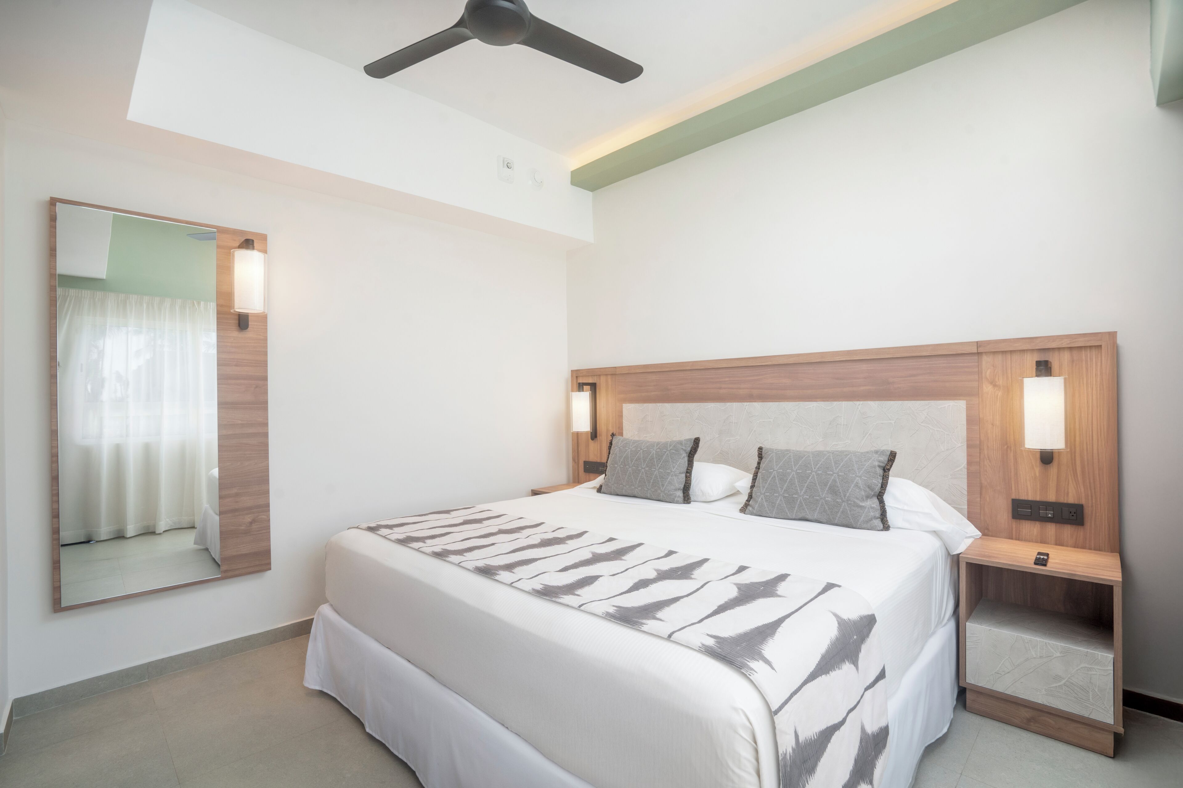 Una habitación de hotel con una cama, mesitas de noche, un espejo y un ventilador de techo.