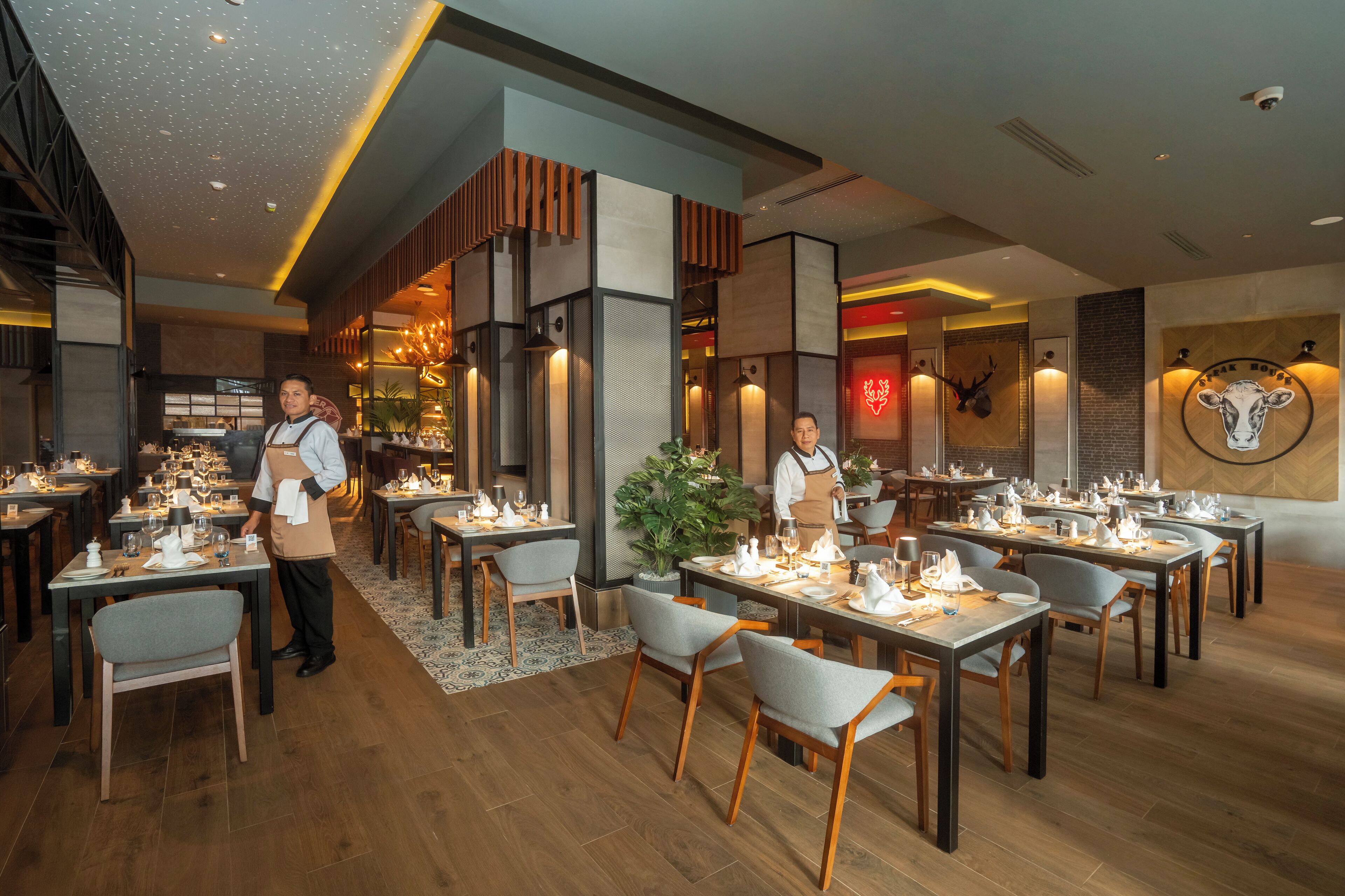 A restaurant with multiple dining tables and chairs, a large potted plant, and a wall with a cow head decoration.