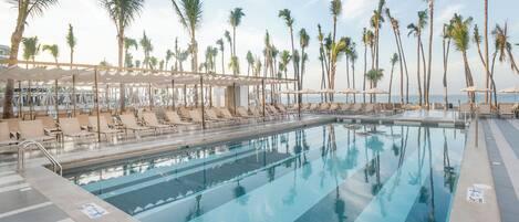A pool area with lounge chairs and umbrellas, surrounded by palm trees.