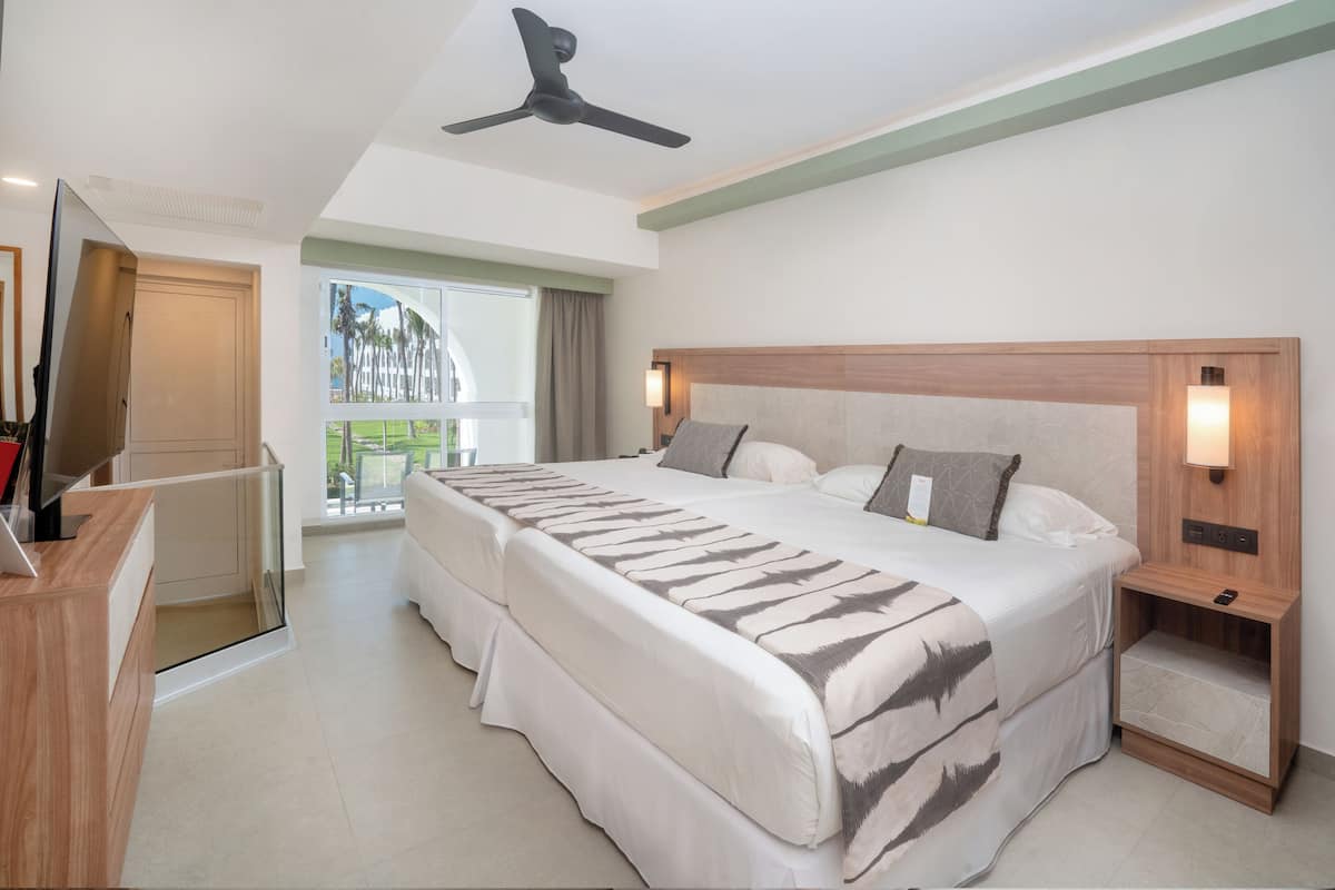 A hotel room with a bed, bedside tables, a desk, a ceiling fan, and a window with a view.