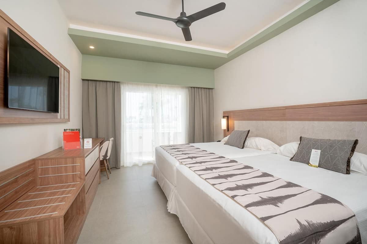 A hotel room with a bed, a desk, a chair, a television, and a ceiling fan.