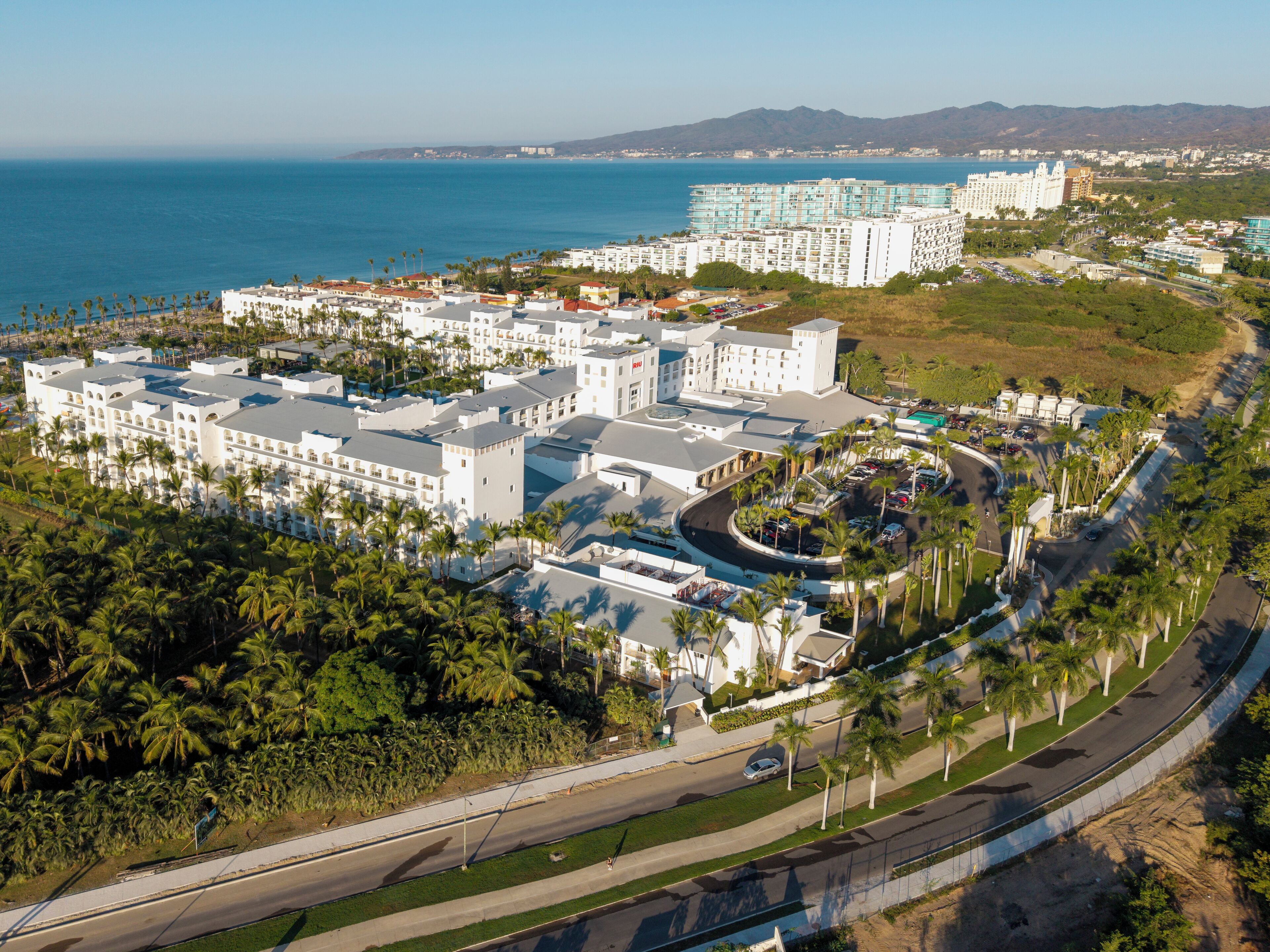 An aerial view of a resort with multiple buildings, a curved road, and a coastline in the background.