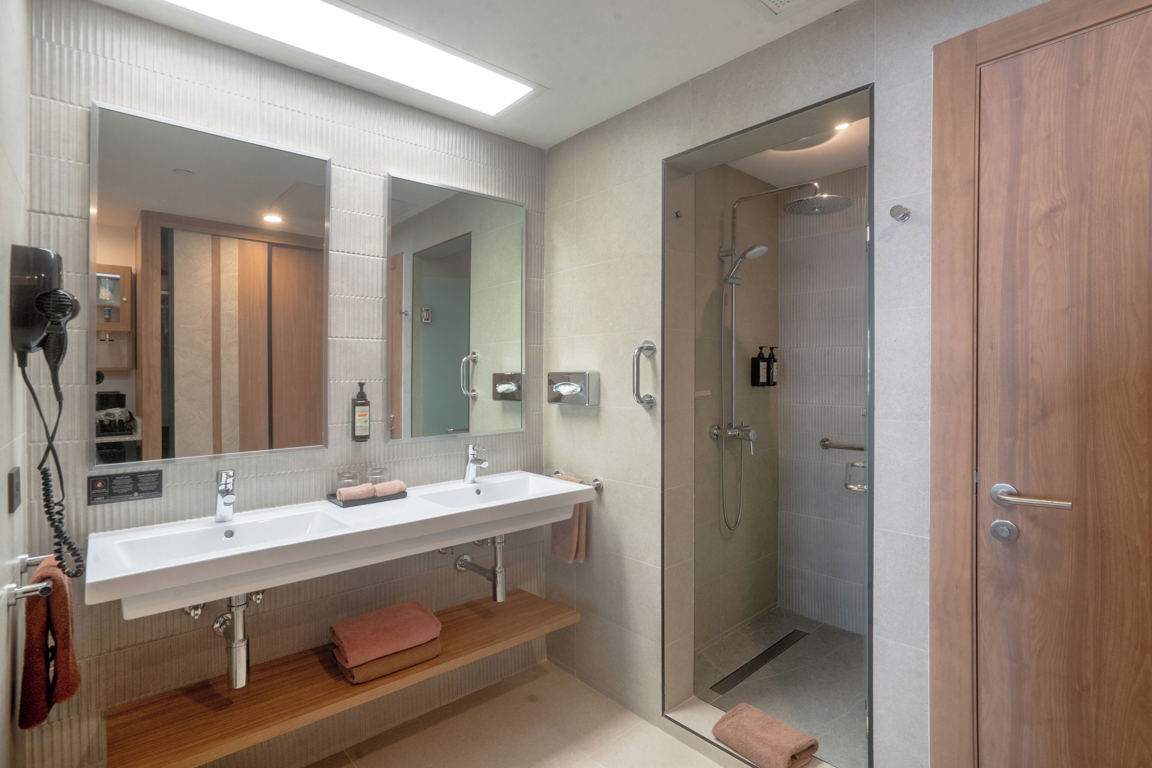 A modern bathroom with a large mirror, two sinks, a shower, and a wooden vanity.