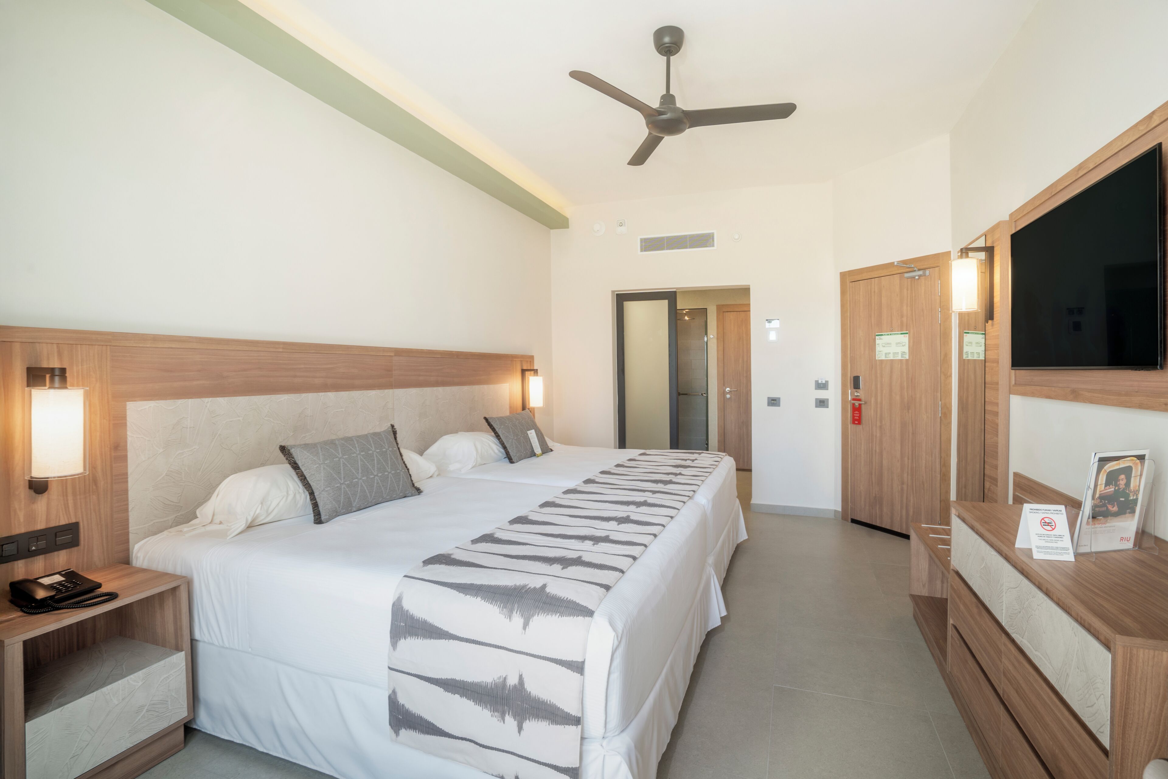 A hotel room with a large bed, bedside tables, a ceiling fan, a mirror, and a reception desk.