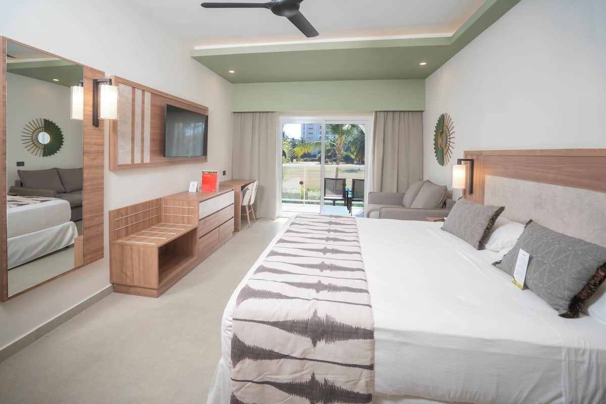 A hotel room with a bed, a TV, a seating area, and a balcony with a view.
