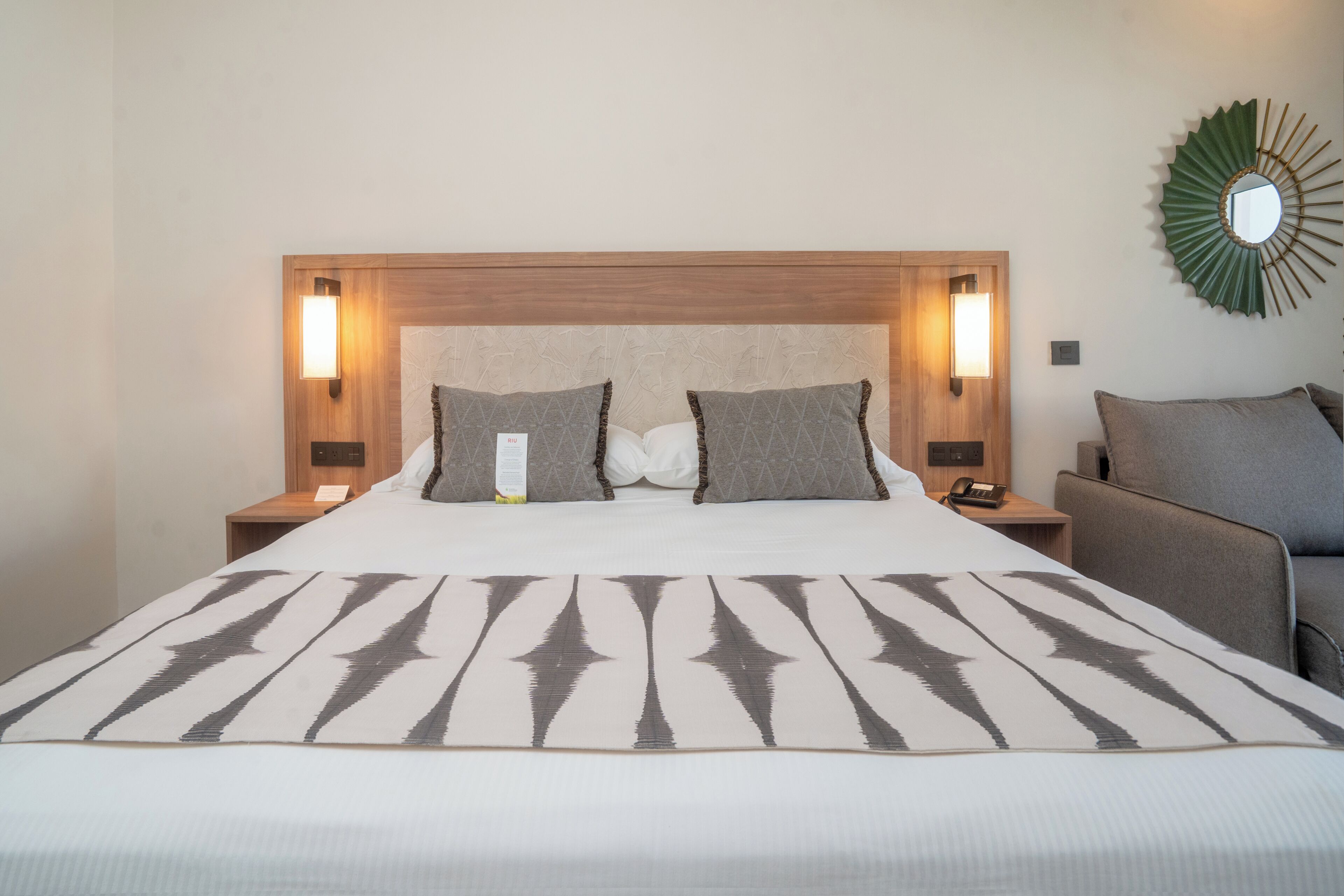 A hotel room with a large bed, two bedside tables, a chair, a wall-mounted mirror, and a decorative wall piece.