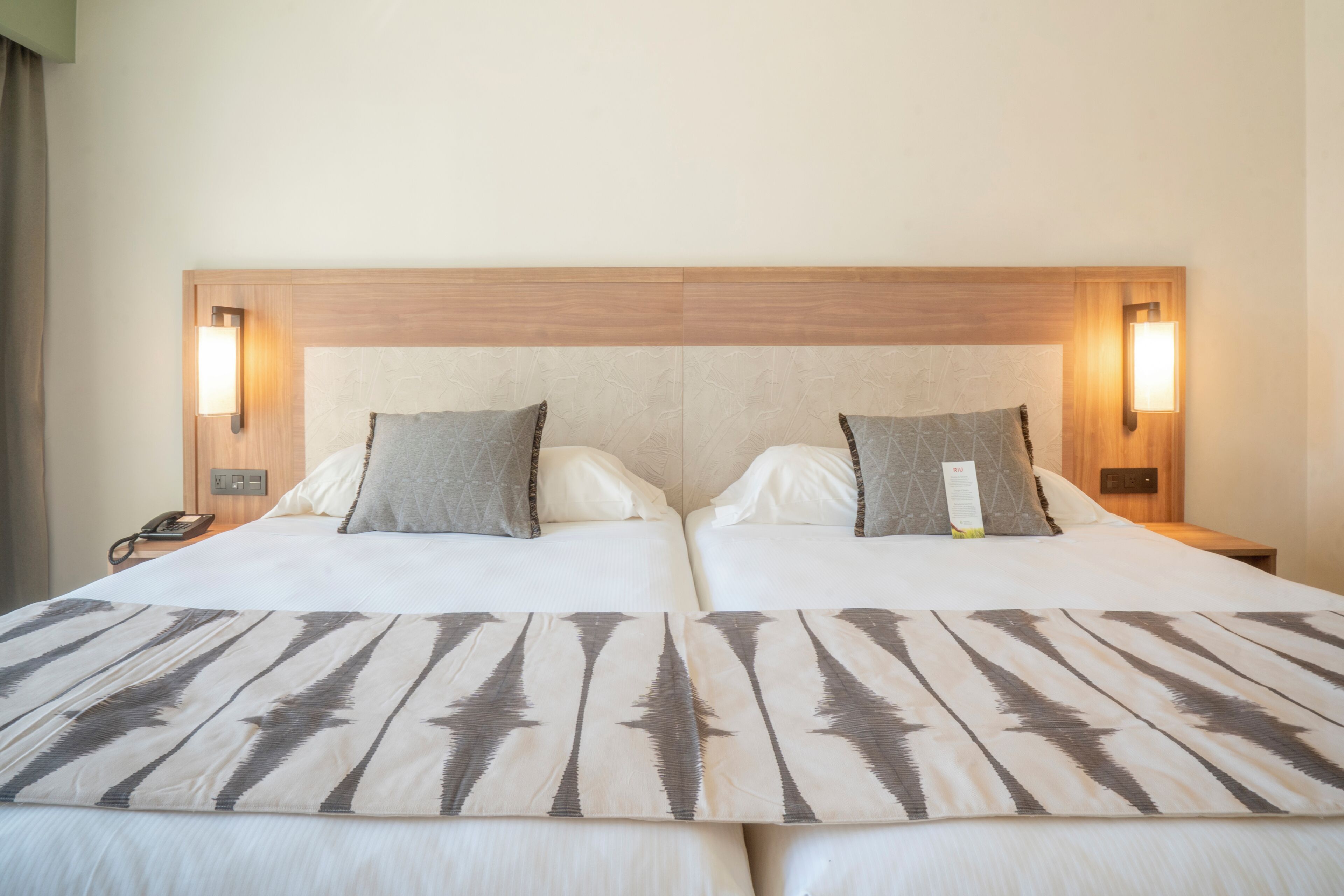 Un lit double avec une tête de lit en bois, deux lampes de chevet et une couvre-lit à motifs.