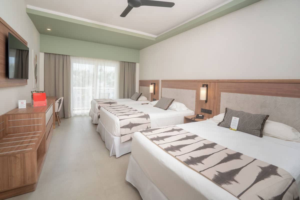 A hotel room with two beds, a desk, a television, and a ceiling fan.