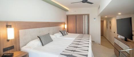 Una habitación de hotel con una cama grande, mesitas de noche, un ventilador de techo, televisor y armario.