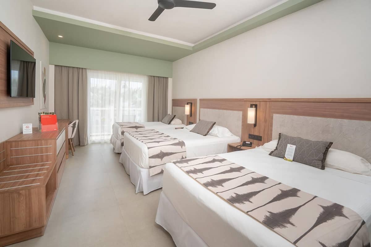 A hotel room with two beds, a desk, a television, and a ceiling fan.
