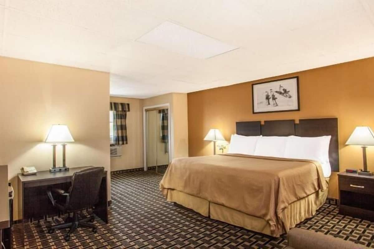 A hotel room with a bed, desk, chair, television, lamps, and a framed picture on the wall.
