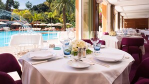A dining area with tables set for a meal, overlooking a pool with lounge chairs and umbrellas. - Es Saadi Marrakech Resort Hotel (Marrakech)