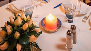 A dining table set for two with a candle, salt and pepper shakers, and a glass of water. - Es Saadi Marrakech Resort Hotel (Marrakech)