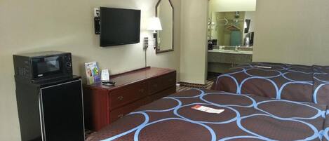 A hotel room with a bed, a dresser, a microwave, a television, and a bathroom mirror.