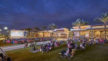 An outdoor movie screening area with a large screen, seating, and palm trees.