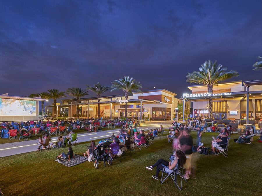 An outdoor movie screening area with a large screen, seating, and palm trees.