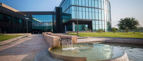 A modern building with a glass facade, a central courtyard with a water feature, and a well-maintained lawn.