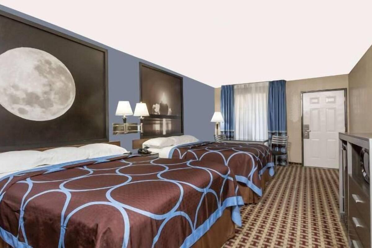 A hotel room with two beds, a large moon mural, a television, and a desk.