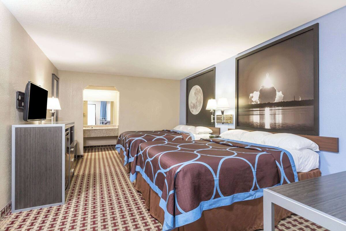 A hotel room with two beds, a desk, a TV, and a large window with a cityscape view.