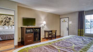 Una habitación de hotel con cama, televisión, escritorio con lámpara, silla y puerta.